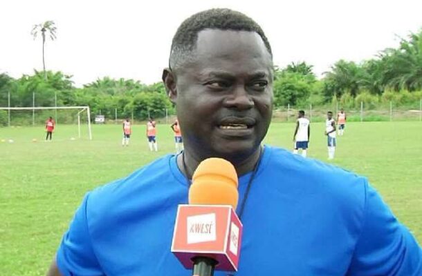 IMG_1026 | Ghanaguardian.com Man in a blue shirt speaks into an orange KWESA microphone on a soccer field, with players practicing in the background.