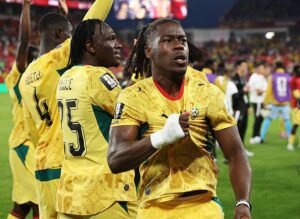 Group of soccer players in yellow jerseys celebrate on the field, foreground player fist-pumping in celebration.