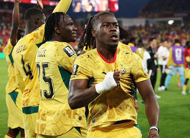 Group of soccer players in yellow jerseys celebrate on the field, foreground player fist-pumping in celebration.