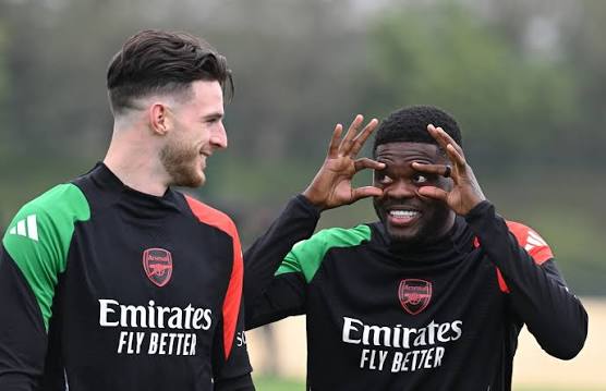 Two Arsenal players in training kits on a field, smiling and talking together.