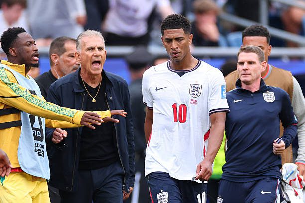 England soccer players on the field with a coach shouting at a player in a white England jersey numbered 10 nearby.