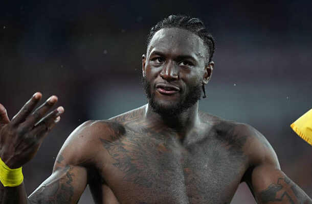 IMG_1053 | Ghanaguardian.com Shirtless athletic man with cornrow braids and chest tattoos gesturing on a sports field in a dim setting.