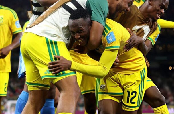 Soccer players in yellow and green celebrate a goal, embracing each other on the field during a match at night.