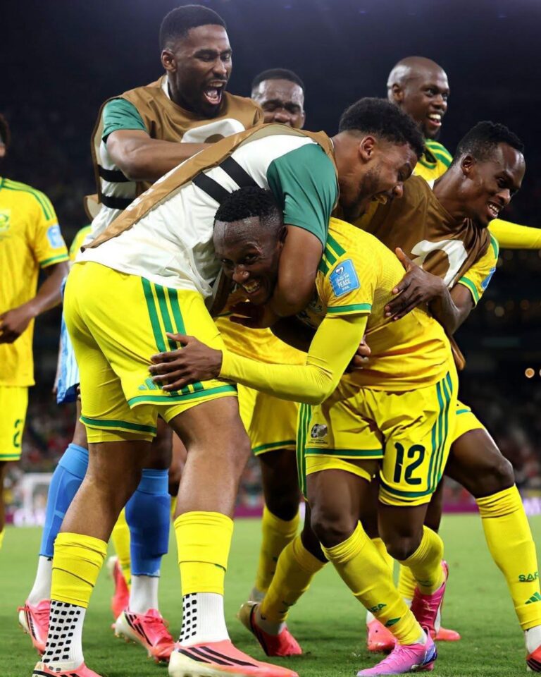 Soccer players in yellow and green celebrate a goal, embracing each other on the field during a match at night.