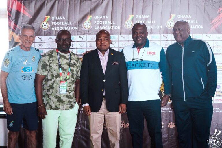 Five men stand in front of a Ghana Football Association backdrop posing for a photo at an event.