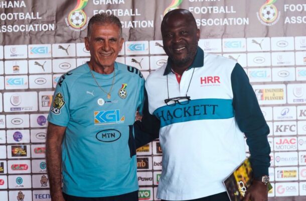 Two men posing together at a Ghana Football Association event backdrop, wearing team jerseys.