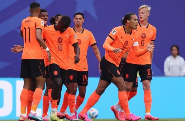 Group of Netherlands football players celebrating together on the pitch in bright orange jerseys.