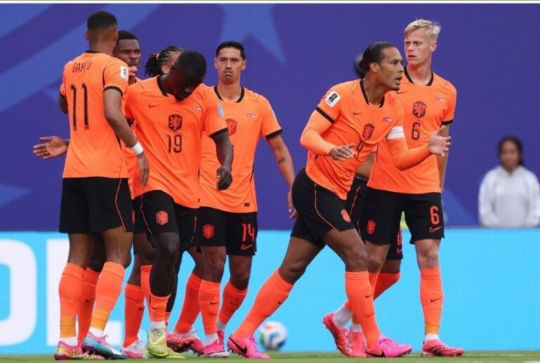 Group of Netherlands football players celebrating together on the pitch in bright orange jerseys.