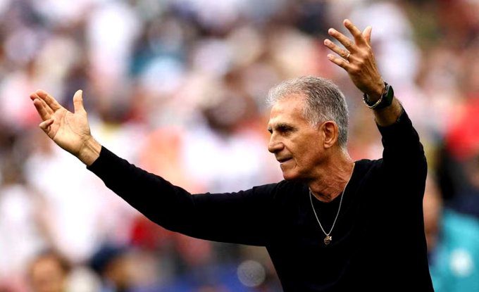 Man with gray hair in a black shirt waving to a cheering crowd in a stadium setting.