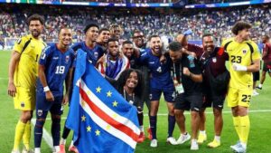 A national football team posing with a flag on the field after a match, smiling and celebrating together.