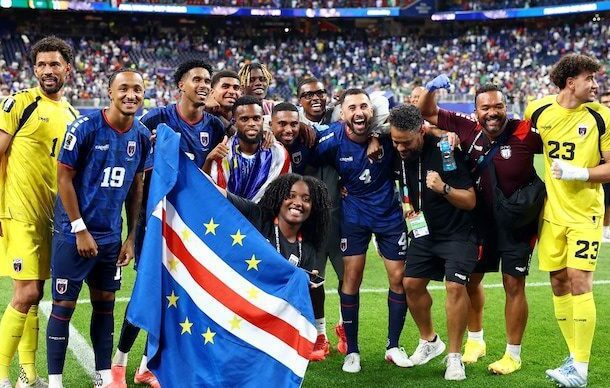 A national football team posing with a flag on the field after a match, smiling and celebrating together.