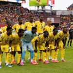 Senegal national football team in yellow kits posing for a pre-match group photo on the field, goalkeeper in light blue, with a crowded stadium in the background.