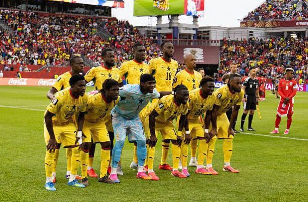 Senegal national football team in yellow kits posing for a pre-match group photo on the field, goalkeeper in light blue, with a crowded stadium in the background.