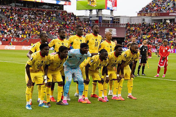Soccer team in yellow uniforms posing for a pre‑match lineup on the field, with a goalkeeper in light blue and a crowded stadium in the background.