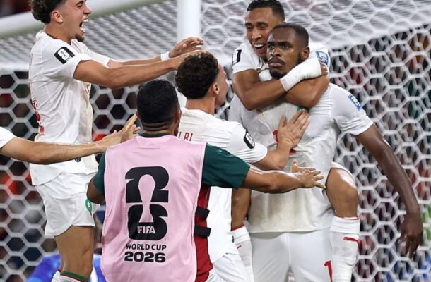 IMG_1127 | Ghanaguardian.com Group of soccer players in white uniforms celebrate a goal by the goal, with one player wearing a pink bib that reads FIFA World Cup 2026 in the foreground, and a net in the background.