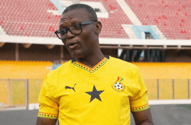 IMG_1134 | Ghanaguardian.com Man in a bright yellow soccer jersey with a black star on the chest, speaking or gesturing on a stadium field.
