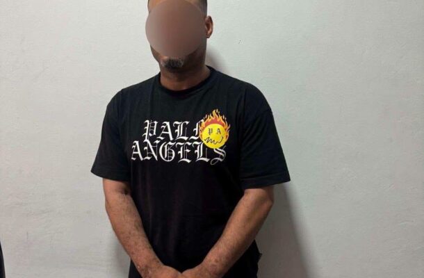Kwadwo Akofena Safo | Ghanaguardian.com Man in a black T-shirt with a flame logo and 'HELl ANGELS' text, standing against a light gray wall with face blurred for privacy.