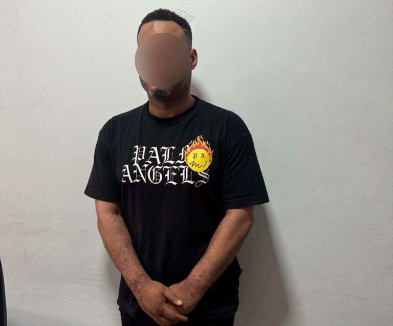 Man in a black T-shirt with a flame logo and 'HELl ANGELS' text, standing against a light gray wall with face blurred for privacy.