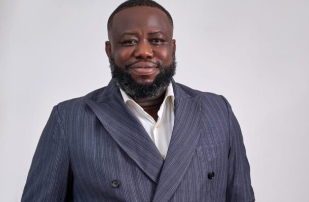Michael Kpakpo Allotey | Ghanaguardian.com Smiling man in a navy pinstripe double-breasted suit and white shirt against a light gray studio background.