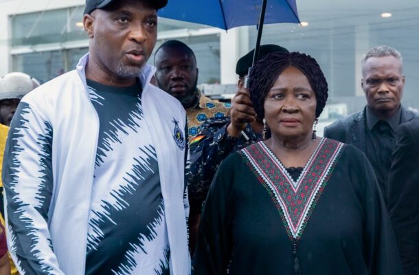 Muntaka Mubarak 12 | Ghanaguardian.com Man in a white and teal patterned jacket and a woman in a black traditional dress stand in the rain under a blue umbrella.