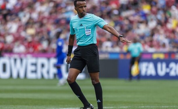 Omar-Artan-vsb-1835-341f47-750x375 | Ghanaguardian.com Soccer referee in turquoise shirt and black shorts signaling on a green pitch as fans watch in the stands.
