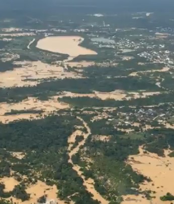 Aerial view of a sandy coast with winding riverlike channels and clusters of green vegetation, with a small town visible in the distance.