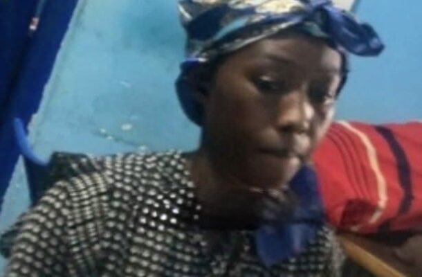 Person wearing a black-and-white patterned blouse and a blue headwrap sits in a blue room with a calendar on the wall behind them.