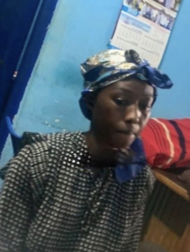 Person wearing a black-and-white patterned blouse and a blue headwrap sits in a blue room with a calendar on the wall behind them.