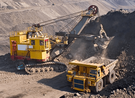 Yellow hydraulic mining excavator loading earth into a heavy dump truck at an open-pit quarry, dust rising around the equipment.