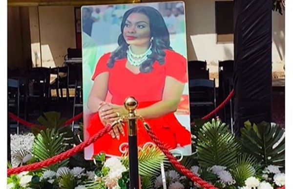 Portrait of a woman in a red dress and pearl necklace on a stand at a roped-off floral display at an event as a centerpiece photo