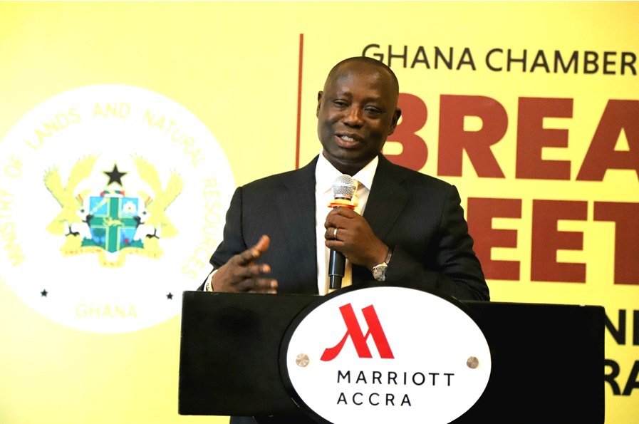 Man in a suit speaking at a podium with a microphone at Marriott Accra, Ghana; banner in the background reads 'Ghana Chamber' and 'Break'.