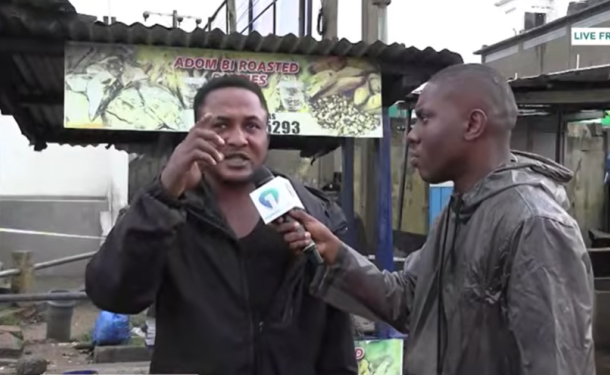 Screenshot-2026-06-07-095516-750x375 | Ghanaguardian.com Man being interviewed on a street, gesturing with his hand while a reporter in a gray hoodie holds a microphone toward him; a roasted food stall sign is visible in the background.
