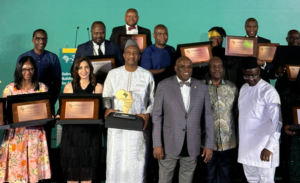 Group of award recipients posing with framed plaques on a stage during a ceremony.