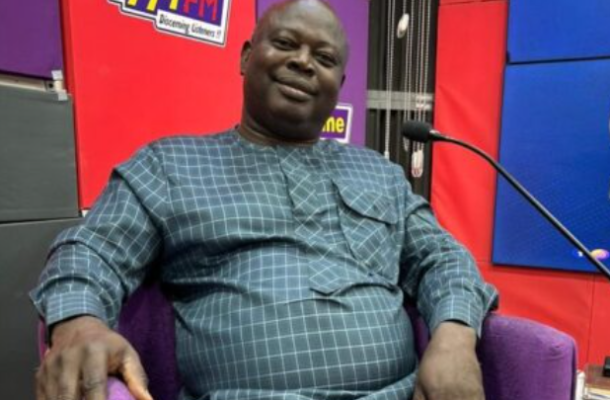 Screenshot-2026-06-16-125022 | Ghanaguardian.com Smiling man in a blue checkered outfit sits in a purple chair in a radio studio with 99.7 FM signage nearby.