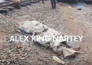 A motionless body covered with a blanket lies on rocky ground at a construction area, with a watermark reading ALEX KING NARTEY across the scene.