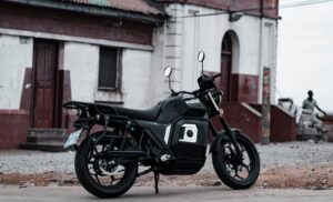 Black and gray motorcycle parked on a gravel street in front of a white building with red trim and doors visible behind it