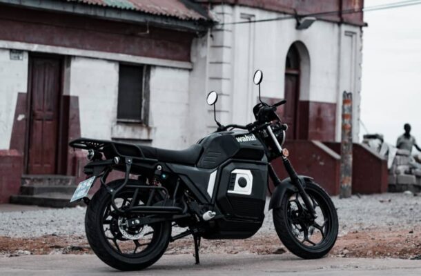 Electric motorcycles | Ghanaguardian.com Black and gray motorcycle parked on a gravel street in front of a white building with red trim and doors visible behind it