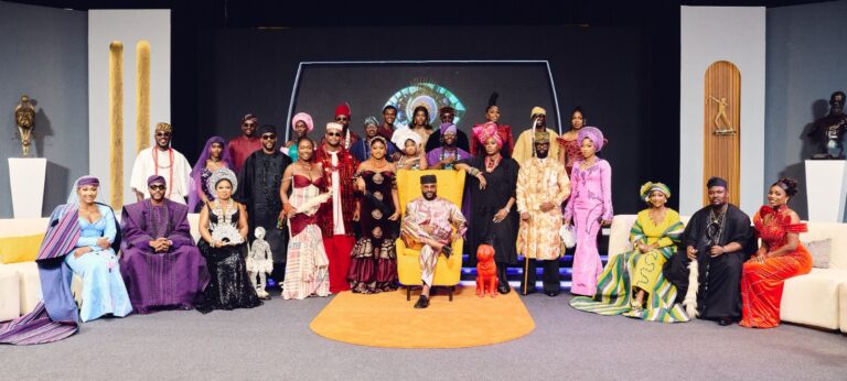 Group photo of men and women in vibrant traditional African attire on a stage, posing for a group portrait.
