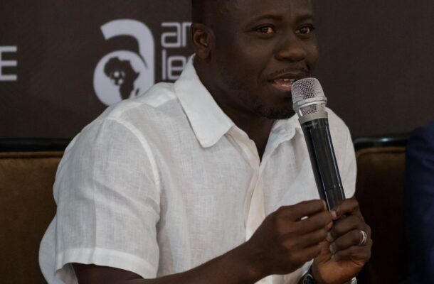 Man in a white short-sleeve shirt speaks into a microphone during a panel discussion.