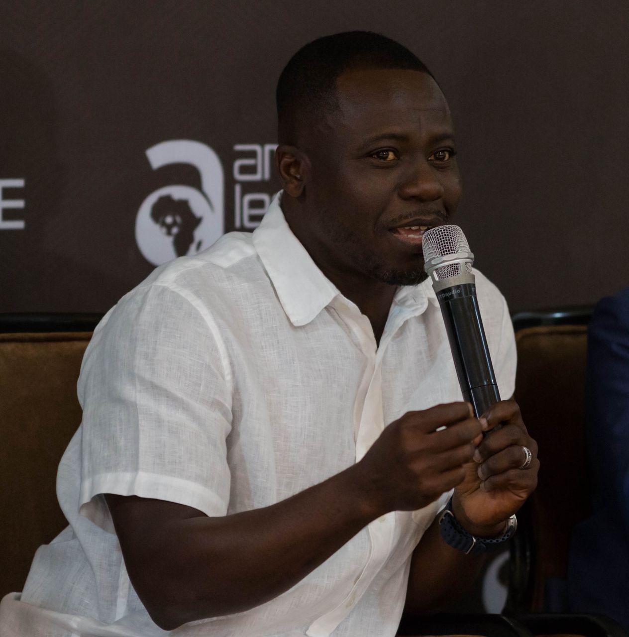 Man in a white short-sleeve shirt speaks into a microphone during a panel discussion.