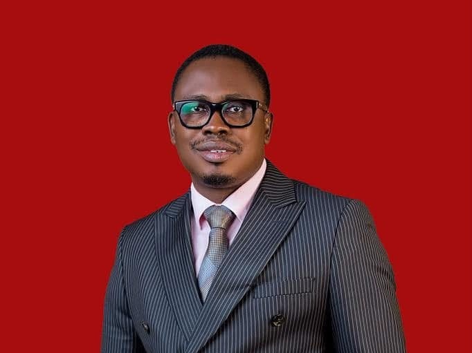 Portrait of a man in a gray pinstripe suit with glasses against a solid red background.