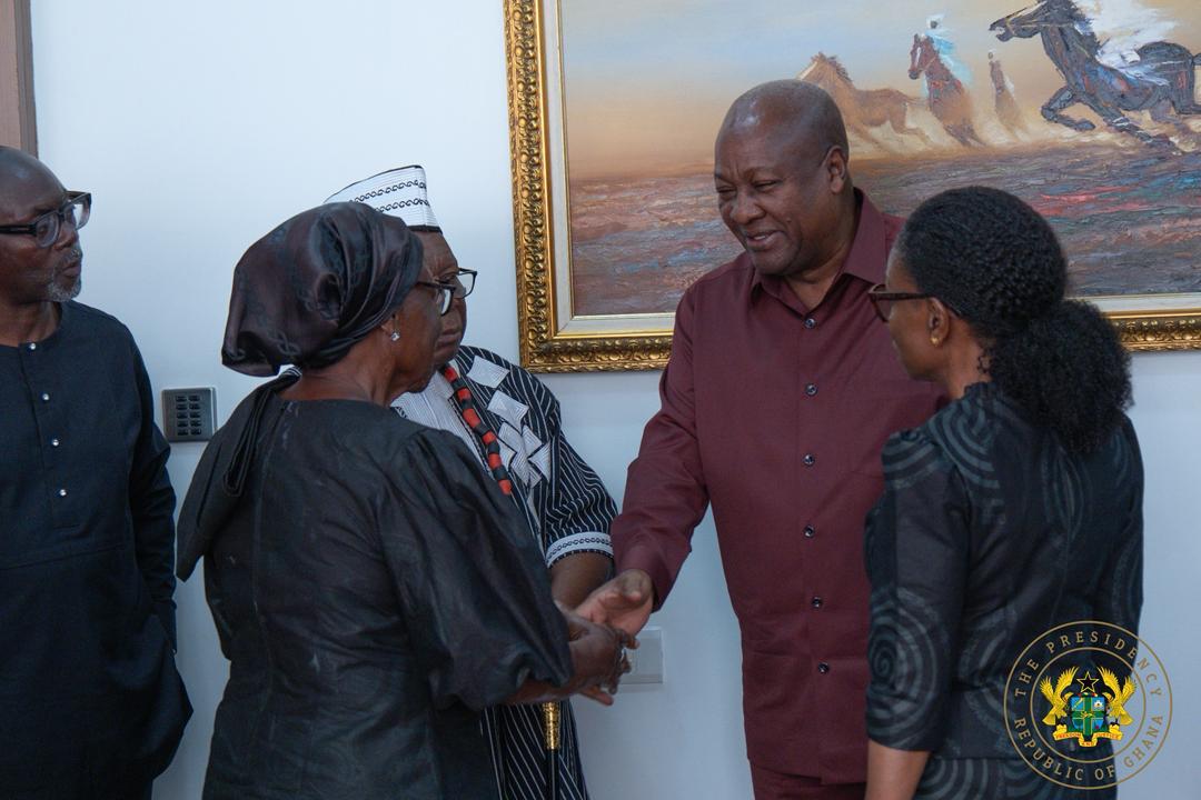 Group of formally dressed people shake hands in a doorway, with a painting behind and an official seal in the corner, suggesting a diplomatic meeting in Ghana.