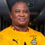 Portrait of a smiling man in a yellow football jersey standing in a dim hallway.