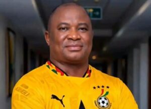 Portrait of a smiling man in a yellow football jersey standing in a dim hallway.