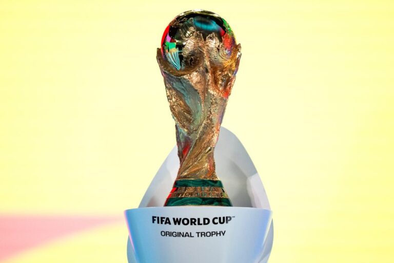 FIFA World Cup Original Trophy displayed on a white stand against a pale yellow background, front view core details visible