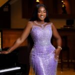 Woman in a sparkling lavender evening gown standing at a grand piano in a dimly lit lounge, smiling at the camera