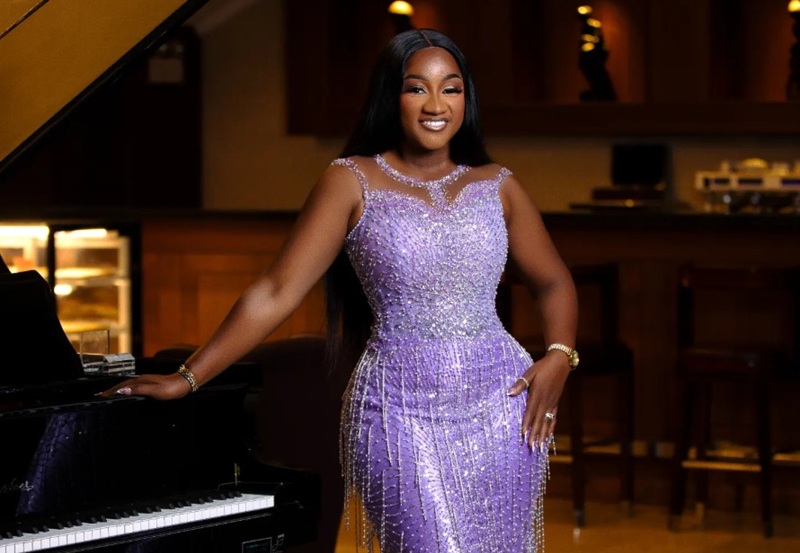 Woman in a sparkling lavender evening gown standing at a grand piano in a dimly lit lounge, smiling at the camera