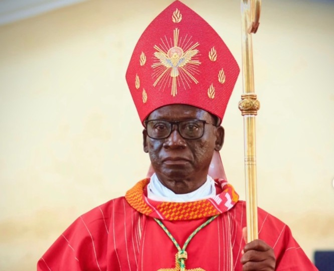 Catholic bishop wearing a red mitre and robe, holding a ceremonial staff during a liturgical ceremony.