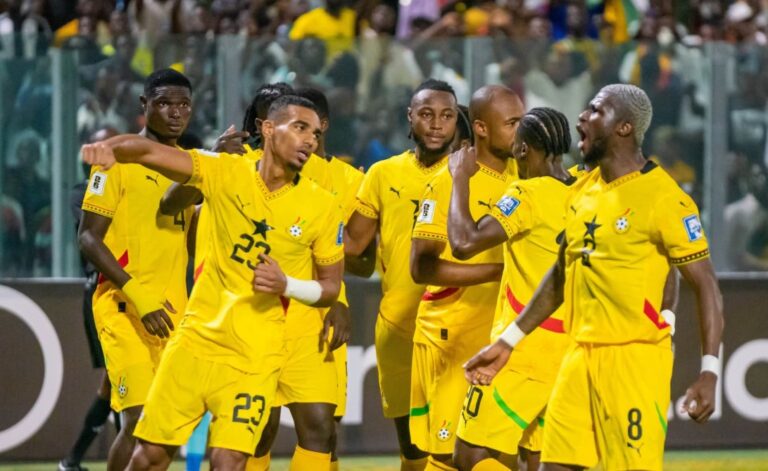 A group of soccer players in bright yellow uniforms celebrate on the field as teammates high-five and gesture, with fans in the stands behind them.