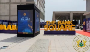 Promotional display reading THE BANK SQUARE with large orange letters at an outdoor event; blue info panels nearby and the presidential seal in the bottom-right corner.